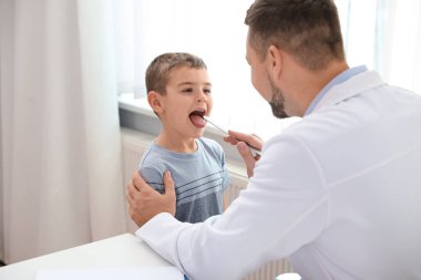 Çocuk doktoru klinikte küçük bir hastanın boğazını muayene ediyor.