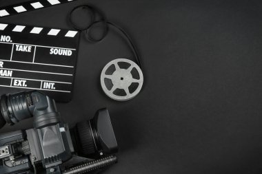 Modern video kamera, film alkışı ve siyah arka planda bobin, düz konum. Metin için boşluk