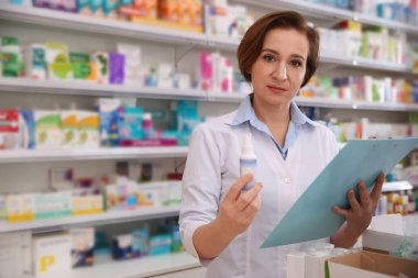 Professional pharmacist with clipboard and medicine in drugstore clipart