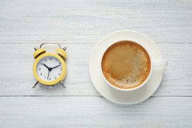 Bir fincan sabah kahvesi ve çalar saat beyaz ahşap masa, düz uzanmış