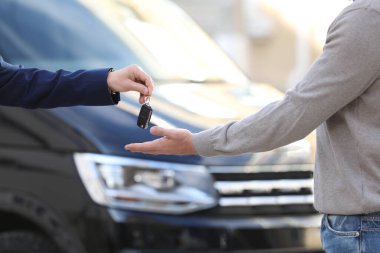 Satıcı, modern oto galerisinde müşteriye anahtar veriyor, yakın plan. Yeni araba alınıyor