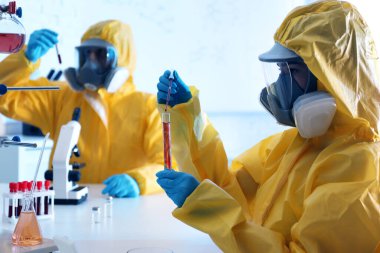 Kimyasal koruyucu kıyafetli bilim adamı laboratuardaki test tüpüne kan damlatıyor. Virüs araştırması