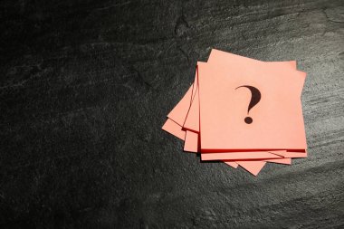 Siyah taş masa üzerinde soru işareti olan pembe kâğıt kartlar, üst manzara. Metin için boşluk