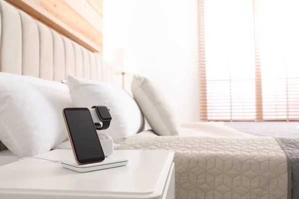 Different gadgets charging on wireless pad in bedroom. Space for text