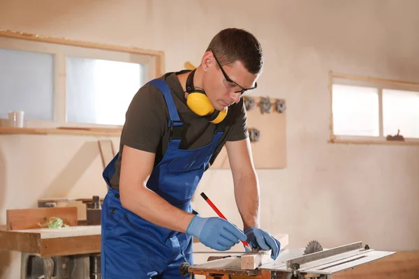 Professional carpenter making mark on wooden bar in workshop