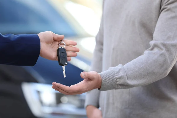 Salesman giving key to customer in modern auto dealership, closeup. Buying new car