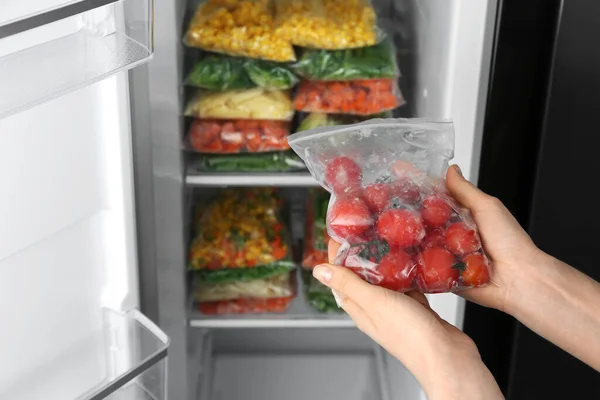 Mujer Sosteniendo Bolsa Plástico Con Tomates Congelados Cerca Refrigerador Abierto —  Fotos de Stock