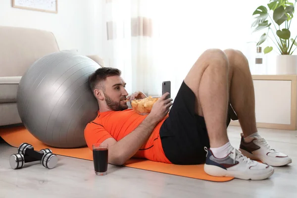 Lazy Ung Man Med Smartphone Äta Skräpmat Yogamattan Hemma — Stockfoto