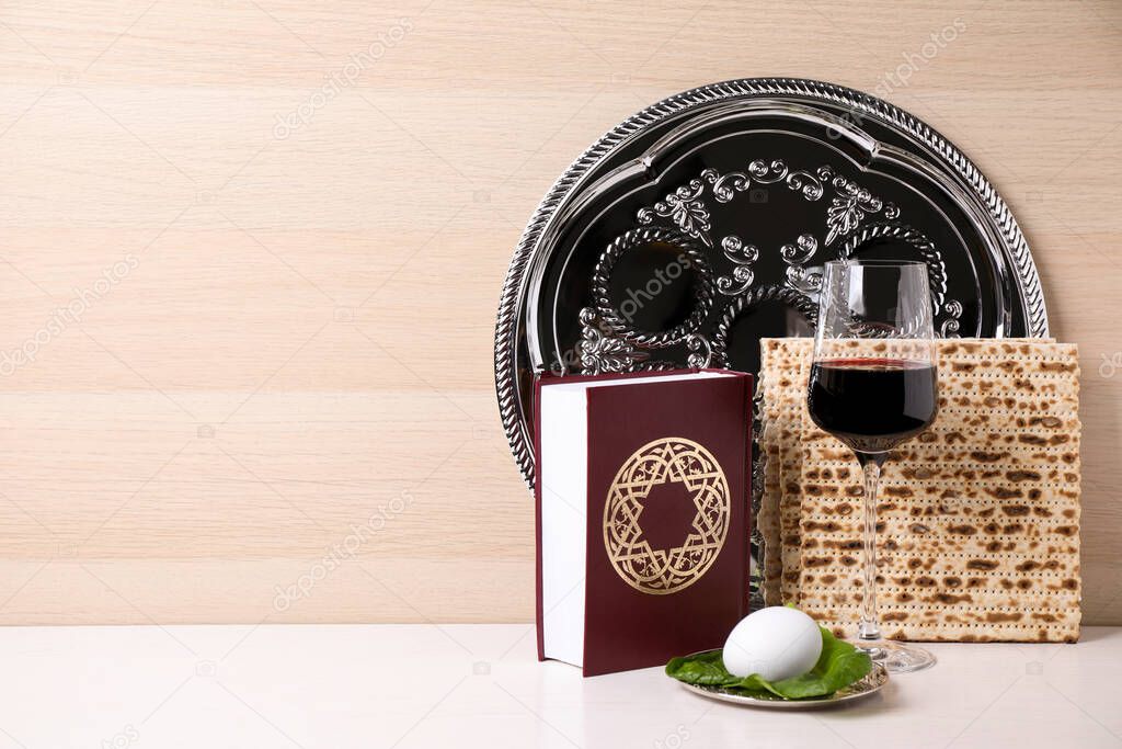 Symbolic Pesach (Passover Seder) items on white table against wooden background, space for text