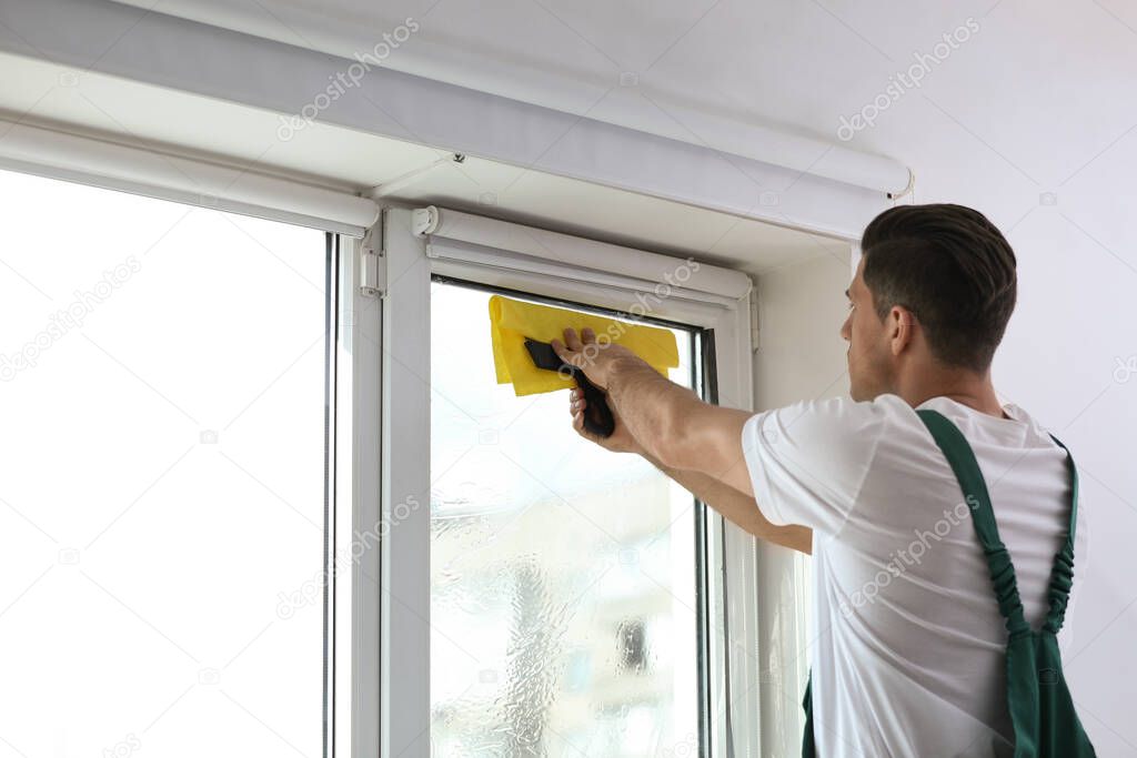 Professional worker tinting window with foil indoors. Space for text