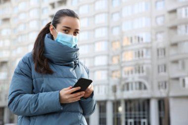 Tek kullanımlık maskeli ve akıllı telefonlu bir kadın. Tehlikeli bir virüs.