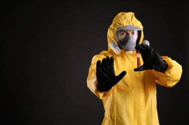 Kimyasal koruyucu giysili bir adam siyah arka planda test tüpü tutuyor, mesaj için yer var. Virüs araştırması