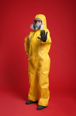 Kimyasal koruyucu elbiseli kadın kırmızı arka planda dur hareketi yapıyor. Virüs araştırması