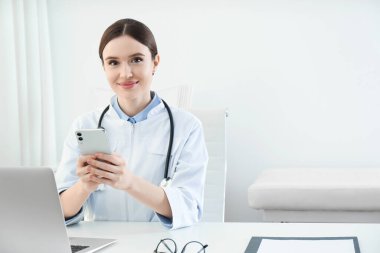Ofisinde akıllı telefonu olan genç bir bayan doktor.