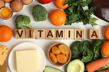 A vitamini ve beyaz ahşap masa üzerinde taze ürünler içeren küp.