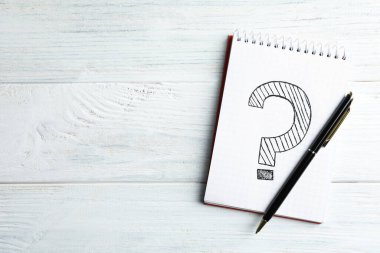 Üzerinde soru işareti ve kalem olan defter beyaz ahşap masa, üst manzara. Metin için boşluk