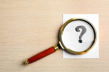 Kağıt kart, üzerinde soru işareti ve büyüteç olan tahta masa, üst manzara. Metin için boşluk