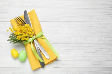 Beyaz ahşap masa üzerinde yumurta ve çiçek dekoru olan çatal bıçak takımının en üst görüntüsü, yazı için yer. Paskalya kutlaması
