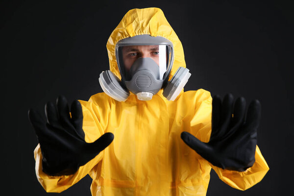 Man in chemical protective suit making stop gesture on black background. Virus research