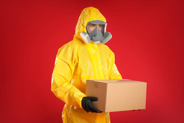 Man wearing chemical protective suit with cardboard box on red background. Prevention of virus spread