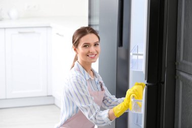 Evde lastik eldivenli bir kadın buzdolabını temizliyor.