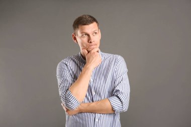 Gri arka planda günlük kıyafetli düşünceli bir adam.