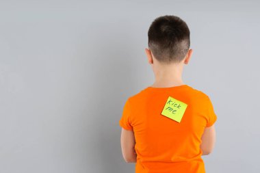 Açık gri arka planda arkasında KICK ME etiketi olan çocuk. 1 Nisan şakası