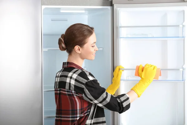 Woman in rubber gloves cleaning refrigerator at home