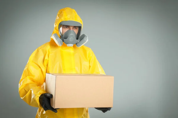薄いグレーの背景に段ボール箱付きの化学保護スーツを着た男 ウイルスの拡散防止 — ストック写真