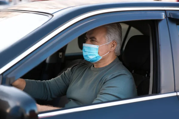 Senior man with medical mask in car. Virus protection