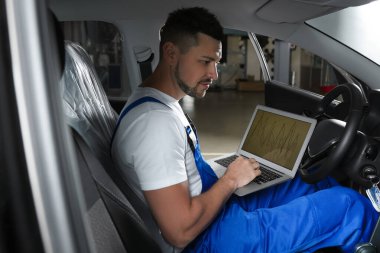 Mechanic with laptop doing car diagnostic at automobile repair shop