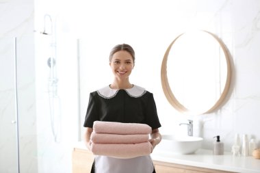 Genç oda hizmetçisi banyoda bir yığın temiz havlu tutuyor.