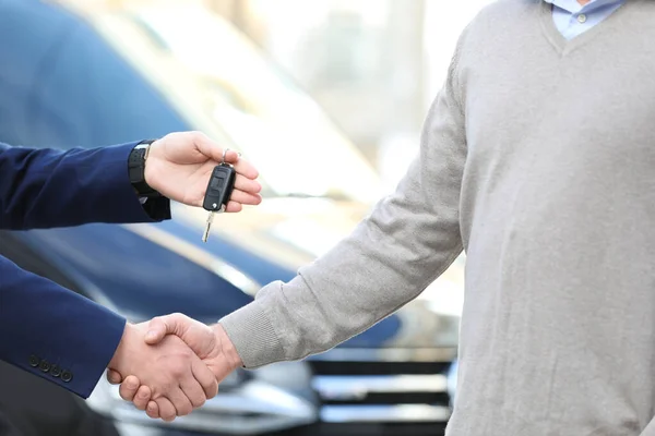 セールスマンは 最新の自動車販売代理店で握手をしながら 顧客に鍵を与えます 新車を買う — ストック写真