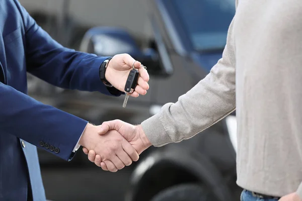 セールスマンは 最新の自動車販売代理店で握手をしながら 顧客に鍵を与えます 新車を買う — ストック写真