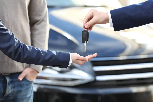 Salesman giving key to customers in modern auto dealership, closeup. Buying new car