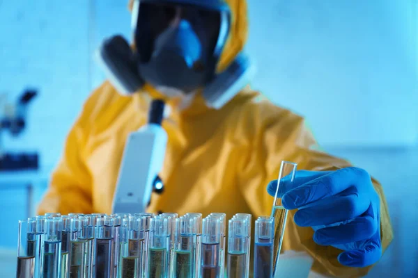 Scientist in chemical protective suit taking test tube out of rack at laboratory, focus on hand. Virus research