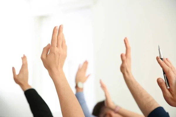 People raising hands to ask questions at business training on light background, closeup