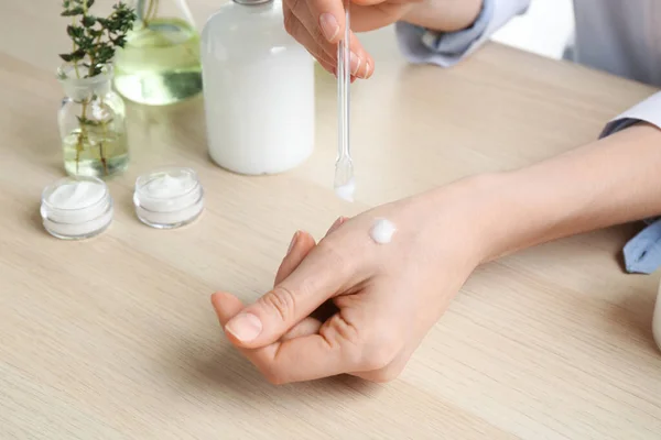 Woman applying natural cream onto hand in cosmetic laboratory, closeup