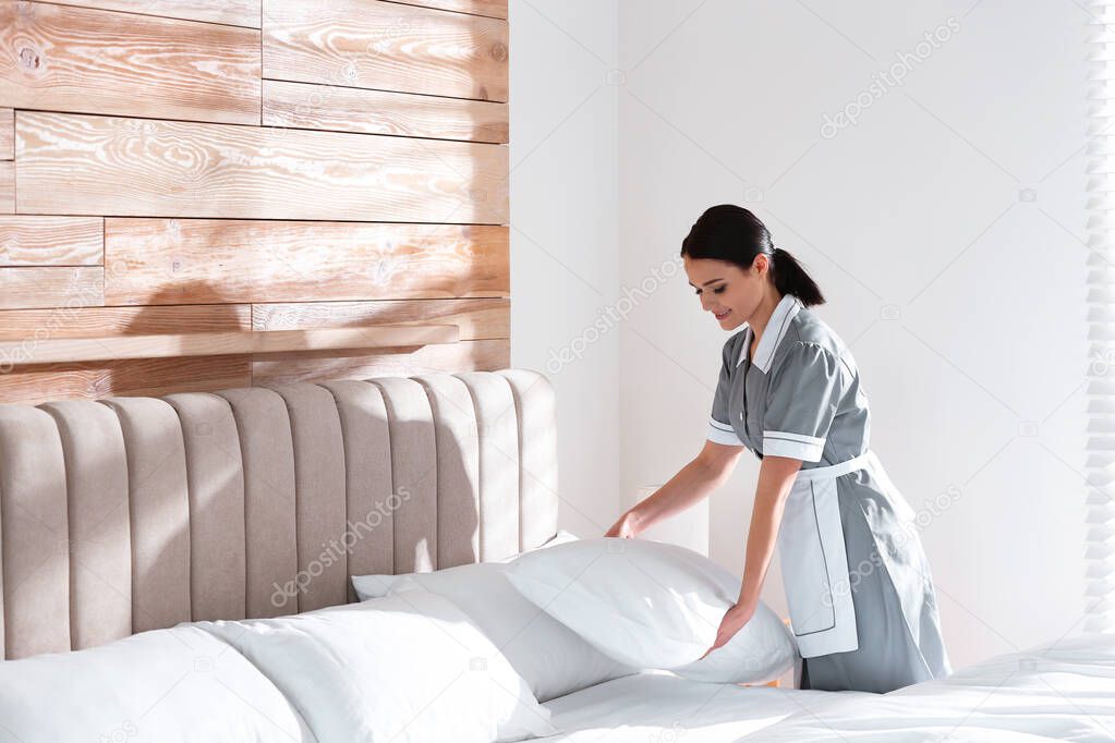 Young chambermaid making bed in hotel room. Space for text