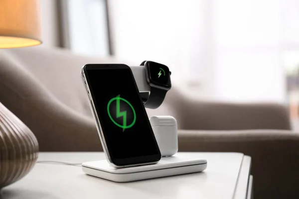 Smartphone, watch and earphones charging on wireless pad in room