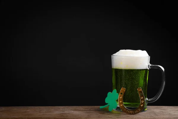 Green beer and clover on wooden table against black background, space for text. St. Patrick\'s Day celebration