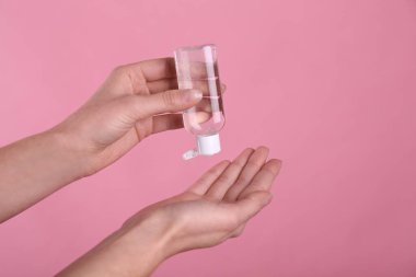 Pembe arka plana antiseptik jel süren kadın, yakın plan.