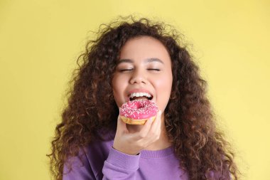 Sarı arka planda donutu olan güzel bir Afro-Amerikalı kadın.