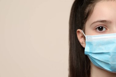 Bej arka planda tıbbi maskeli küçük bir kız, mesaj için yeri olan yakın plan. Virüs koruması