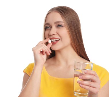 Bir bardak suyla beyaz arka planda vitamin hapı alan genç bir kadın.