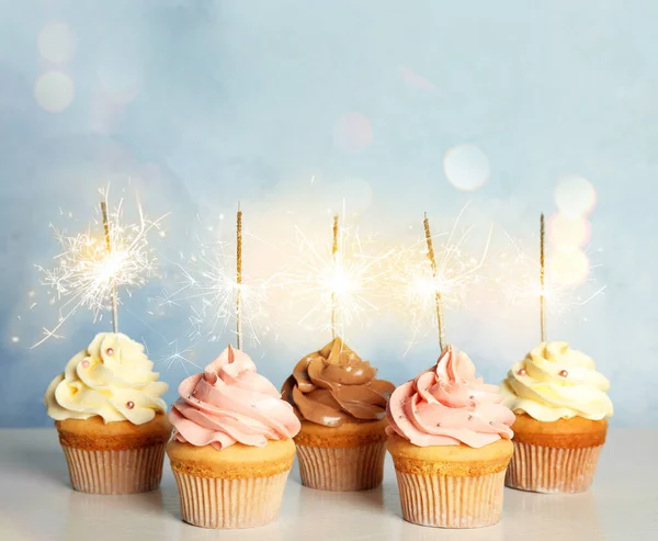 Birthday cupcakes with sparklers on table against light blue background