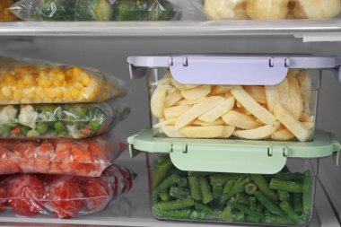 Buzdolabında farklı donmuş sebzeler olan plastik torbalar ve kaplar, yakın plan.