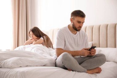 Young man preferring smartphone over his girlfriend on bed at home. Relationship problems clipart