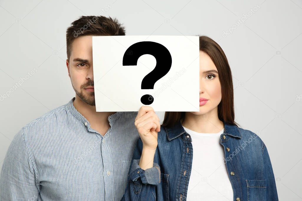 Couple holding question mark sign on light background