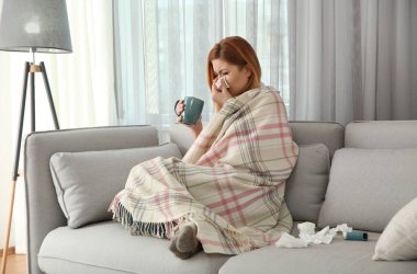 Ekoseye sarılı hasta kadın evde bir fincan sıcak içecekle bekliyor. Grip virüsü